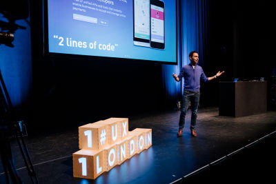 Scott Belsky speaking at the UX London conference. The â€˜UX Londonâ€™ logo in the form of cubes is arranged on the stage next to the speaker